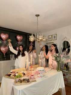 a group of women standing around a table holding up heart shaped balloons and plates with food on it