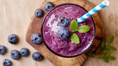 a smoothie with blueberries and mint on a wooden board next to some leaves