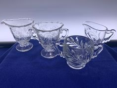 four clear glass cups and saucers on a blue cloth