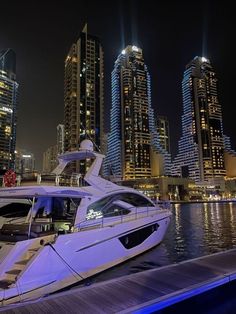 a white boat is docked in front of some tall buildings at night with blue lights