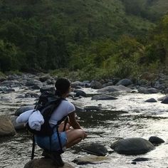 a woman sitting on rocks in the middle of a river with her back to the camera