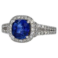 A contemporary sapphire and diamond engagement ring that commands attention. A 1.62 carat cushion cut sapphire is centered displaying a vibrant and deep blue. Accented by over 1 carat of shimmering, icy white diamonds forming the halo and open "V" split band. This design balances out the face of this gemstone engagement ring, spreading the treasured jewels around your finger. The 18 karat white gold band and setting pushes this ring over the top.   Condition: Very Good Era: Contemporary Year: 20 Sapphire And Diamond Engagement Ring, Gemstone Engagement Ring, Bleu Violet, Gemstone Engagement, Sapphire Engagement Ring, La Face, White Gold Band, Split Shank, Sapphire Engagement