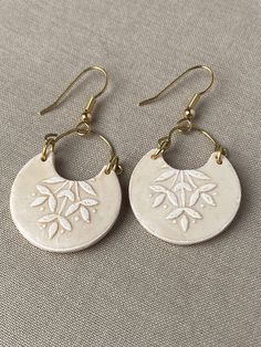 two pairs of earrings with white flowers on them sitting on top of a gray surface