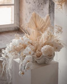 a vase with flowers and feathers on top of a white pedestal in front of a window