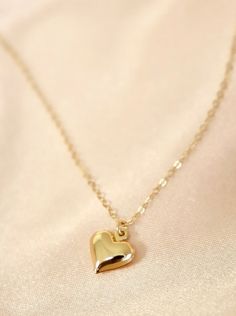 This necklace features a brass-plated puff heart charm on an 18" gold-filled chain. Crafted from premium materials including gold-filled chain and a brass heart charm, this necklace is sure to make a statement. Length: 18" long Gold Heart-shaped Brass Necklace, Heart Shaped Brass Necklaces, Gold-tone Heart Necklace With Adjustable Chain, Gold-tone Heart Pendant Necklace With Adjustable Chain, Brass Heart Charm Pendant Necklace, Delicate Gold Necklace With Heart Charm, Dainty Gold-tone Heart Jewelry, Dainty Heart-shaped Brass Necklaces, Valentine's Day Heart Pendant Necklace With Gold Chain