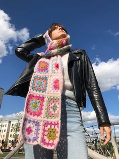 a woman wearing a pink scarf and black leather jacket standing in front of a blue sky