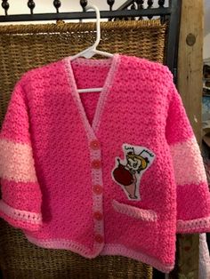 a pink knitted cardigan with a cartoon character on the front and side, hanging from a hanger