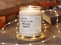 a candle is sitting on a table with string lights around it and the label reads, you're in the bridal party