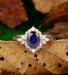 a tan and white ring with a blue stone surrounded by diamonds on top of a leaf