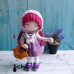 a crocheted doll is holding a basket with purple flowers and a potted plant