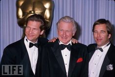 three men in tuxedos are posing for a photo with an oscar statue behind them