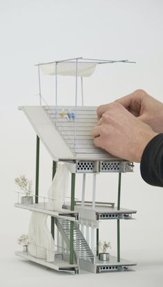 a hand is holding a model of a house with stairs and windows on the roof