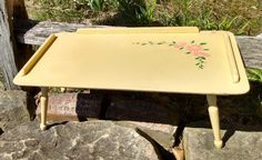 a yellow tray with pink flowers painted on it sitting on some rocks next to a wooden fence