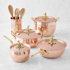 copper pots and pans with gold handles on a marble countertop next to utensils