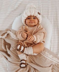 a baby is wearing a knitted hat and holding a stuffed animal in it's lap