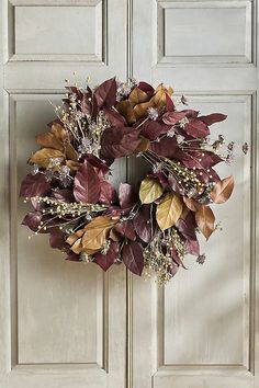 a wreath is hanging on the front door with purple leaves and white flowers in it