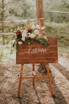 a welcome sign with flowers and greenery on it in the middle of a forest