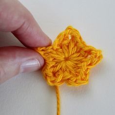 someone is crocheting an orange flower on a white surface with their fingers touching it