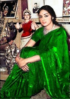 an old photo of a woman in green sari sitting on a couch with statues behind her