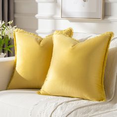 two yellow pillows sitting on top of a white couch next to a potted plant