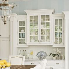 a bowl of lemons sits on a table in the middle of a white kitchen