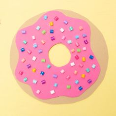 a pink doughnut covered in sprinkles on top of a yellow table