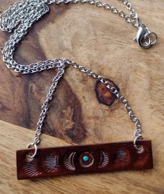 a wooden necklace with metal chains on top of a wood table next to a piece of jewelry