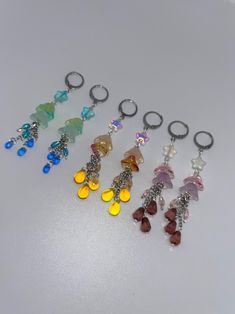 six different colored glass beads hanging from metal rings on a white surface with silver hooks