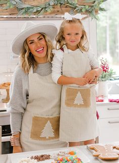 two women in aprons standing next to a table with cookies and doughnuts on it