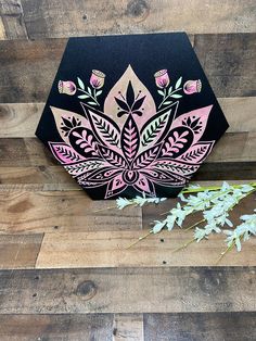 a black box with pink and green designs on it sitting next to some white flowers