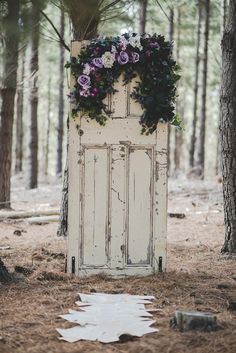 an old door is decorated with flowers and greenery in the middle of a forest