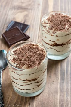 two desserts sitting on top of a wooden table next to a spoon and chocolate bar