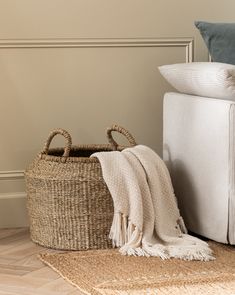 a white couch sitting next to a basket on top of a wooden floor