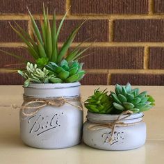 two white mason jars with succulents tied to them on top of a table