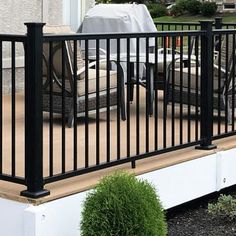 a deck with black iron railings and chairs on it in front of a house