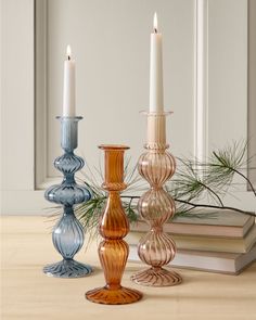 three glass candlesticks sitting on top of a table next to an open book