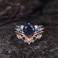 a blue diamond ring sitting on top of a black stone covered ground with leaves and flowers