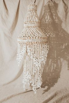 a white beaded chandelier hanging from the ceiling on a beige fabric background