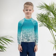 a young boy standing in front of a palm tree wearing a blue and green shirt