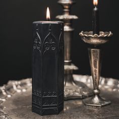 two candles sitting on top of a table next to an ornate silver vase and candle holder