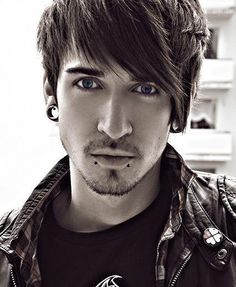 a young man with blue eyes and piercings on his ear looking at the camera