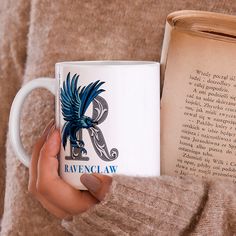 a person holding a coffee mug in front of an open book with raven claw on it