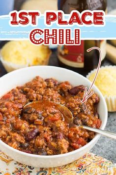 a white bowl filled with chili next to cupcakes and other food on a table