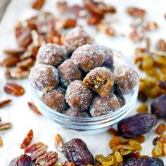 nuts and raisins in a glass bowl on a white surface with other nuts scattered around