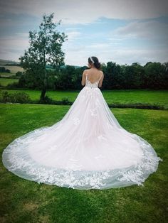 a woman in a wedding dress standing on the grass looking out at the field behind her