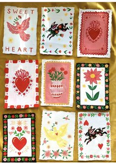 nine embroidered napkins with hearts, flowers and birds on them are sitting on a gold cloth