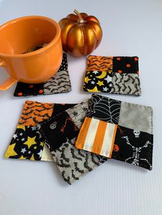 four halloween coasters on a table next to a cup and orange pumpkin in the background