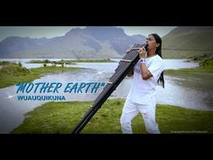 a woman holding a large instrument in front of a body of water with mountains in the background