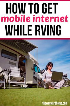 a woman sitting on the grass with her laptop in front of a camper trailer