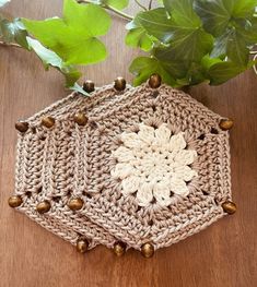 a crocheted pot holder with bells on top of it and a plant in the background